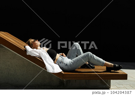 Stylish pretty woman lying on bench at city street. Woman resting at summer day outdoors 104204387
