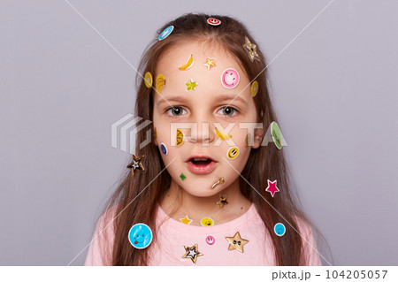 Closeup shot of shocked amazed little brown haired little girl covered with stickers looking at camera with open mouth, sees something surprised, posing isolated over gray background Closeup shot of shocked amazed little brown haired little girl covered with stickers looking at camera with open mouth, sees something surprised, posing isolated over gray background 104205057