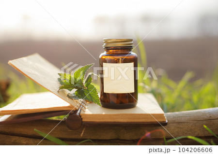 Glass container with natural pills, medicine. Old notepad and medicine container, fresh herbs from the nettle 104206606