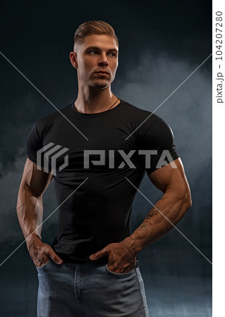 Athletic sexy man in black t-shirt and jeans posing in studio 104207280