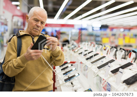 elderly grayhaired man pensioner examining counter with electronic gadgets and tablets in showroom of digital goods store elderly grayhaired man pensioner examining counter with electronic gadgets and tablets in showroom of digital goods store 104207673