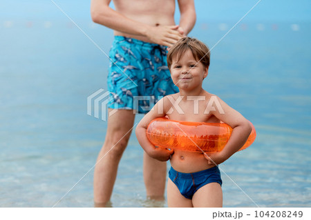 Son and father are standing on the beach after swimming in the sea. The child has an inflatable circle. 104208249