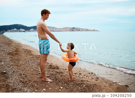 The son calls his father to swim in the sea. Child with inflatable ring. Summer vacation concept 104208250