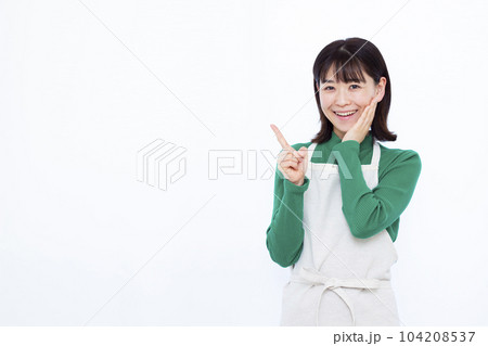 白い背景の前で人差し指を立てるエプロン姿の30代主婦 白い背景の前で人差し指を立てるエプロン姿の30代主婦 104208537