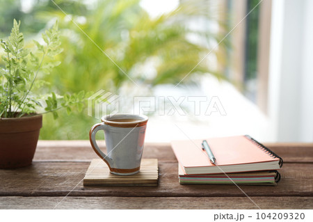 Vintage ceramic coffee cup and notebooks and plant pot on brown wooden table 104209320