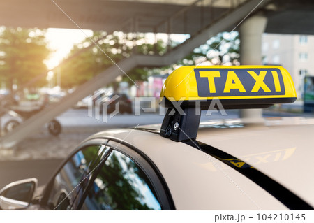 Close-up detail yellow taxi symbol on cars roof stand waiting at parking of airport terminal or railway station against park warm evening bokeh sunlight. Urban street transportation comfort service Close-up detail yellow taxi symbol on cars roof stand waiting at parking of airport terminal or railway station against park warm evening bokeh sunlight. Urban street transportation comfort service 104210145
