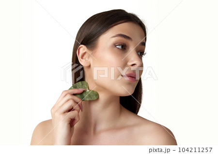 Beautiful young woman with well-kept healthy skin taking care after face with cosmetological massage tool against white studio background 104211257