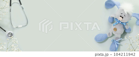 Kids health care banner. Cute knitted toy rabbit with a stethoscope on blue background with white flowers. Family doctor or pediatrician concept. Banner size. Copy space for text Kids health care banner. Cute knitted toy rabbit with a stethoscope on blue background with white flowers. Family doctor or pediatrician concept. Banner size. Copy space for text 104211942
