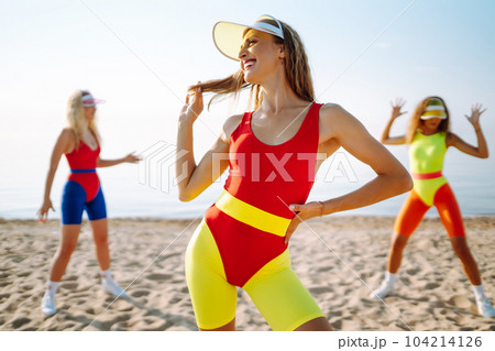 Beautiful women in swimsuits are dancing on beach. Fitness, training, aerobics and people concept. Beautiful women in swimsuits are dancing on beach. Fitness, training, aerobics and people concept. 104214126