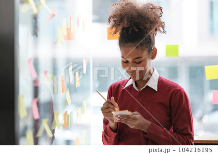 African American female employee write down on colorful sticky notes manage list, concentrated biracial woman work on startup brainstorm collaborate plan on stickers on glass wall African American female employee write down on colorful sticky notes manage list, concentrated biracial woman work on startup brainstorm collaborate plan on stickers on glass wall 104216195