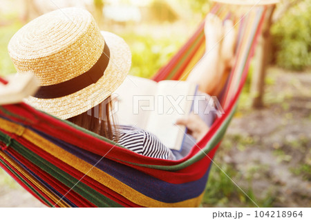 Young woman reading book while lying in comfortable hammock at green garden Young woman reading book while lying in comfortable hammock at green garden 104218964