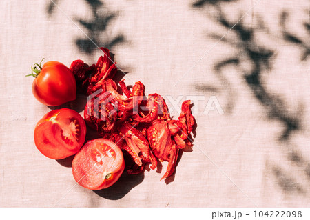 Fresh and dried tomatoes lie on the kitchen table, bright sunlight and shade, top view. Harvesting and processing of vegetables 104222098