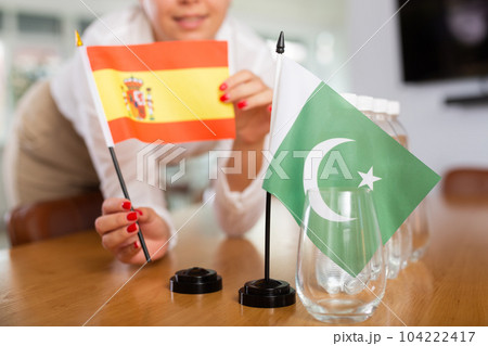Little flag of Pakistan on table and flag of Spain put next to it by young woman 104222417