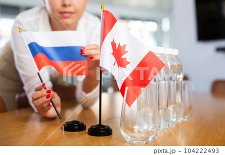 Young woman puts flags of Russia and Canada on table in office Young woman puts flags of Russia and Canada on table in office 104222493