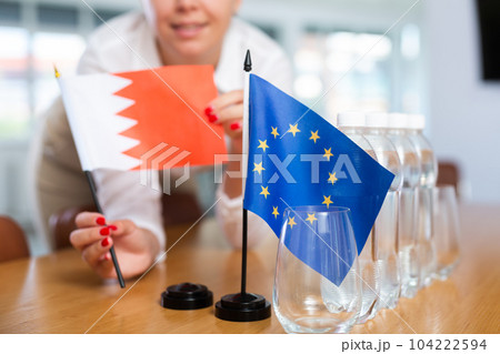 Female secretary places flags of Bahrain and European Union flag on the table before negotiations of top political figures 104222594