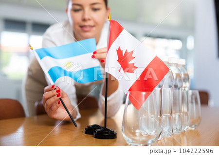 Young woman putting flags of Argentina and Canada on table in office Young woman putting flags of Argentina and Canada on table in office 104222596