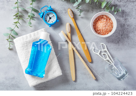 Dental heath care concept, toothbrush with mouthwash, floss, pink salt and clock on grey table with plant, flatlay Dental heath care concept, toothbrush with mouthwash, floss, pink salt and clock on grey table with plant, flatlay 104224423
