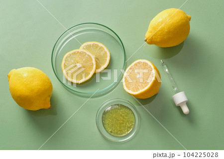 Top view of fresh lemon and lemon slices decorated on a green background with petri dish container essence and dropper. Concept of natural cosmetics with lemon 104225028