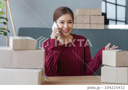 Cheerful small online business owner processing Internet store order for shipping, typing on laptop, speaking mobile phone, using gadgets for communication with clients 104225432