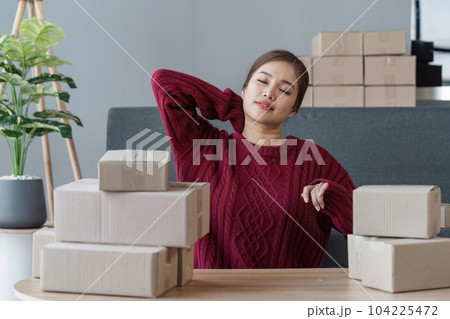 Small online business owner Asian woman stressed headache taking notes with parcel box at home 104225472