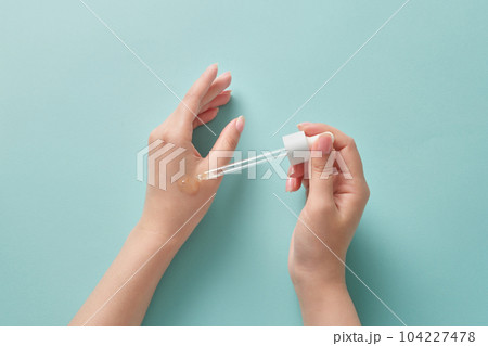 A pretty woman hand model holding a dropper to apply essence on another hand. Natural cosmetics for skin care concept A pretty woman hand model holding a dropper to apply essence on another hand. Natural cosmetics for skin care concept 104227478