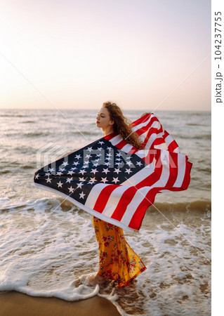Young woman with american flag on the beach at sunset. 4th of July. Independence Day. Young woman with american flag on the beach at sunset. 4th of July. Independence Day. 104237755