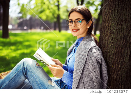 Beautiful relaxed woman readingbook at lawn with sun shining. Girl gets pleasure from reading book. Beautiful relaxed woman readingbook at lawn with sun shining. Girl gets pleasure from reading book. 104238077