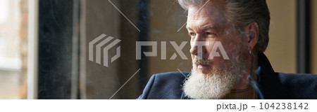 Portrait of thoughtful bearded mature businessman holding cigar and a glass of whisky while relaxing in loft interior 104238142