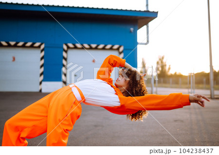 Young African American woman - dancer dancing in the street at sunset. Stylish woman with curly hair in an orange suit showing some moves 104238437