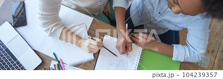 Top view of mixed race teen girl doing math task, school homework together with female teacher in the living room at home 104239357