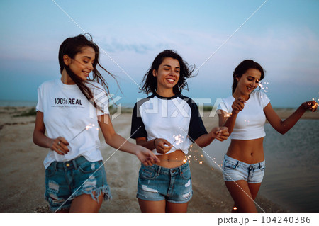 Three beautiful girls celebrating, holding sparklers on the beach at night. . Summer holidays, vacation. Three beautiful girls celebrating, holding sparklers on the beach at night. . Summer holidays, vacation. 104240386