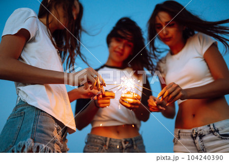 The sparklers in the hands of young girls on the beach. Three girls enjoying party on beach with sparklers. 104240390