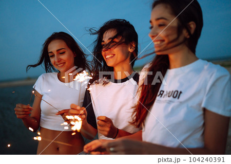 The sparklers in the hands of young girls on the beach. Three girls enjoying party on beach with sparklers. The sparklers in the hands of young girls on the beach. Three girls enjoying party on beach with sparklers. 104240391