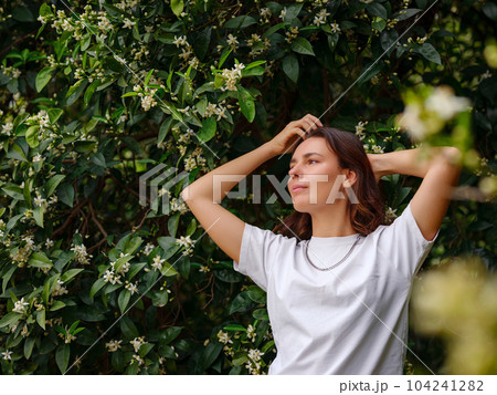 young woman wearing white tshirt posing near blooming flowers in garden. young woman wearing white tshirt posing near blooming flowers in garden. 104241282