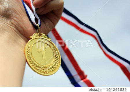 Blurred of woman hands raised and holding gold medals with Thai ribbon against blue sky background to show success in sport or business, Winners success award concept. Blurred of woman hands raised and holding gold medals with Thai ribbon against blue sky background to show success in sport or business, Winners success award concept. 104241823