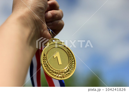 Blurred of woman hands raised and holding gold medals with Thai ribbon against blue sky background to show success in sport or business, Winners success award concept. Blurred of woman hands raised and holding gold medals with Thai ribbon against blue sky background to show success in sport or business, Winners success award concept. 104241826