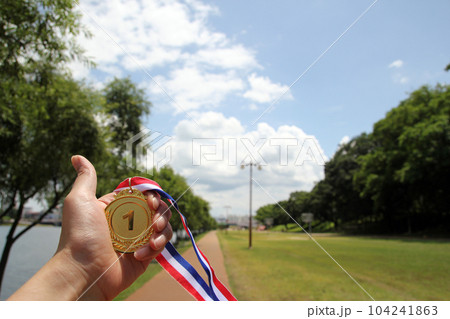 Blurred of woman hands raised and holding gold medals with Thai ribbon against blue sky background to show success in sport or business, Winners success award concept. 104241863