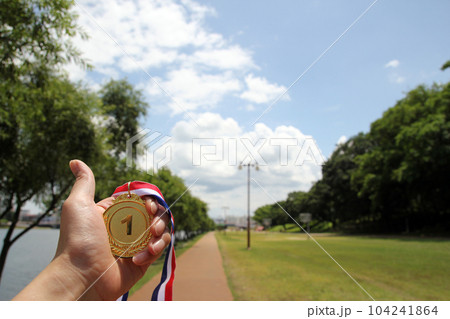 Blurred of woman hands raised and holding gold medals with Thai ribbon against blue sky background to show success in sport or business, Winners success award concept. 104241864