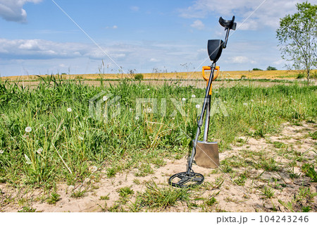 crossed metal detector and shovel on country road in field. tools for searching for treasures and finds 104243246