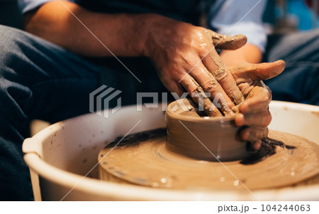 Craftsman potter making jug of clay on the potter's wheel circle in workshop 104244063