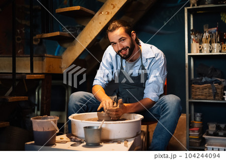 Craftsman potter making jug of clay on the potter's wheel circle in workshop 104244094