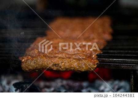 Making Spicy seekh kebabs are being grilled on burning charcoal in barbeque at a dinner party at night 104244381