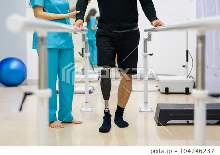 Physiotherapist helping patient with prosthetic leg at parallel bars Physiotherapist helping patient with prosthetic leg at parallel bars 104246237