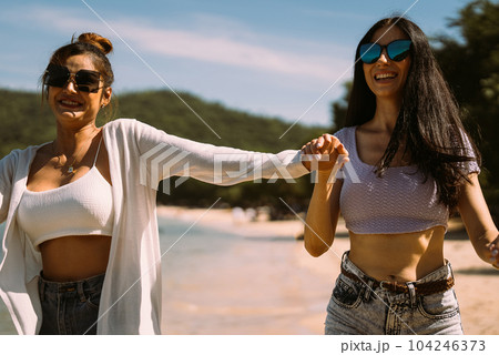 Portrait of two young female friends walking on sea shore happily Portrait of two young female friends walking on sea shore happily 104246373