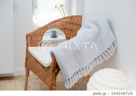 Wicked armchair in minimalist cozy white room interior. Cup of coffee and flowers on the windowsill, beauty and simplicity of morning routine, light scandinavian home interior. Wicked armchair in minimalist cozy white room interior. Cup of coffee and flowers on the windowsill, beauty and simplicity of morning routine, light scandinavian home interior. 104248720