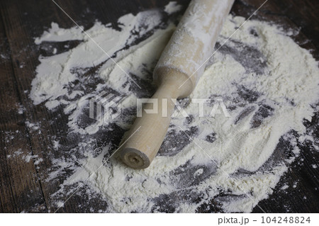 Wooden light rolling pin for dough lies in flour on a dark wooden table. Flour for dough on countertop in kitchen 104248824