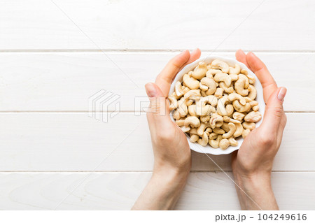 Woman hands holding a wooden bowl with cashew nuts. Healthy food and snack. Vegetarian snacks of different nuts Woman hands holding a wooden bowl with cashew nuts. Healthy food and snack. Vegetarian snacks of different nuts 104249616