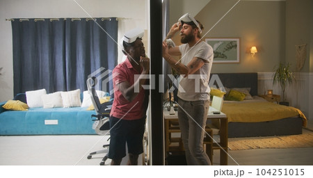 Mixed race men in VR headsets argue through thin walls 104251015