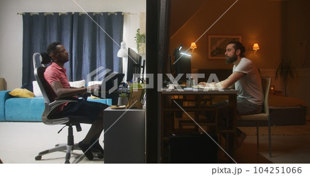 Two multiracial men sit in front of computers in bedrooms Two multiracial men sit in front of computers in bedrooms 104251066