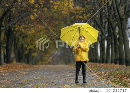 Boy in yellow raincoat with large yellow umbrella walks through the autumn park. Happy child Boy in yellow raincoat with large yellow umbrella walks through the autumn park. Happy child 104252717
